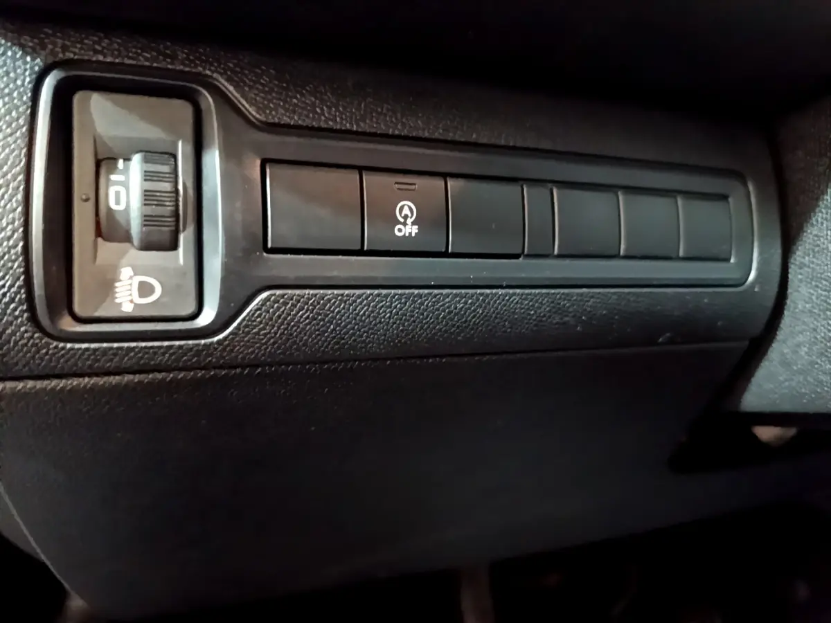 Gros plan sur les commandes de réglage des phares et désactivation du start-stop, intérieur noir de la Peugeot 308 gris clair.