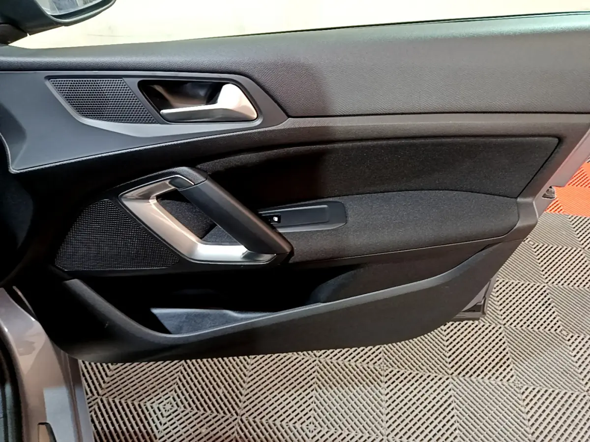 Gros plan sur la porte côté gauche de la Peugeot 308 gris clair, mettant en valeur la poignée intérieure et les haut-parleurs intégrés.