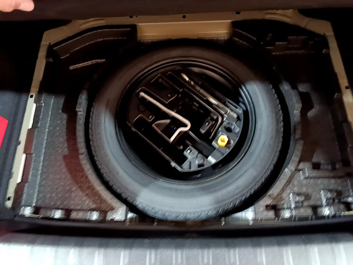 Vue plongeante sur la roue de secours et les outils de bord dans le coffre d'une Peugeot 308 gris clair 2020.