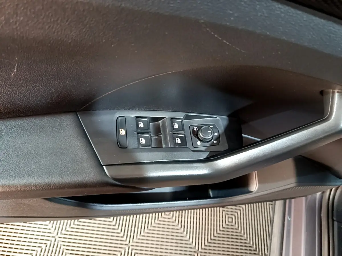 Vue rapprochée des commandes de lève-vitres et réglage des rétroviseurs sur la porte côté gauche du Volkswagen T-Cross gris foncé.