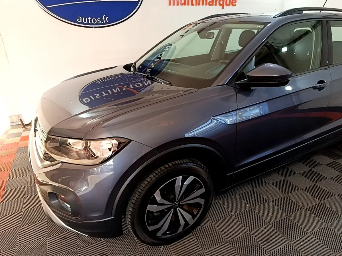 Vue 3/4 avant droit du Volkswagen T-Cross gris foncé 2023 avec jantes noires et toit noir.