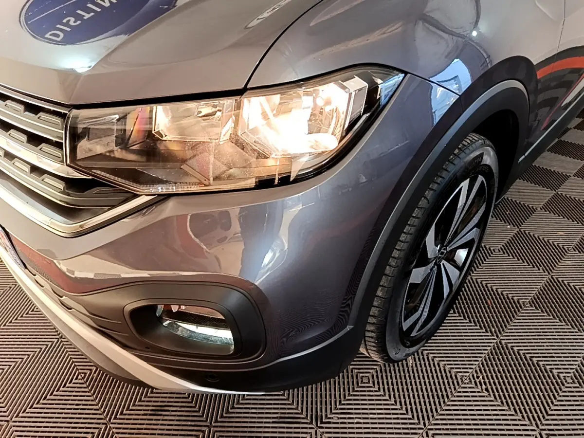 Gros plan sur l'avant droit du Volkswagen T-Cross gris foncé, mettant en valeur le phare allumé et la roue.