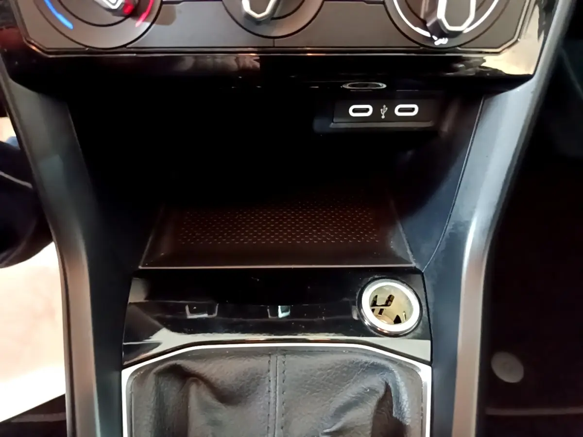 Vue rapprochée de la console centrale noire du Volkswagen T-Cross avec prises USB et allume-cigare visible.