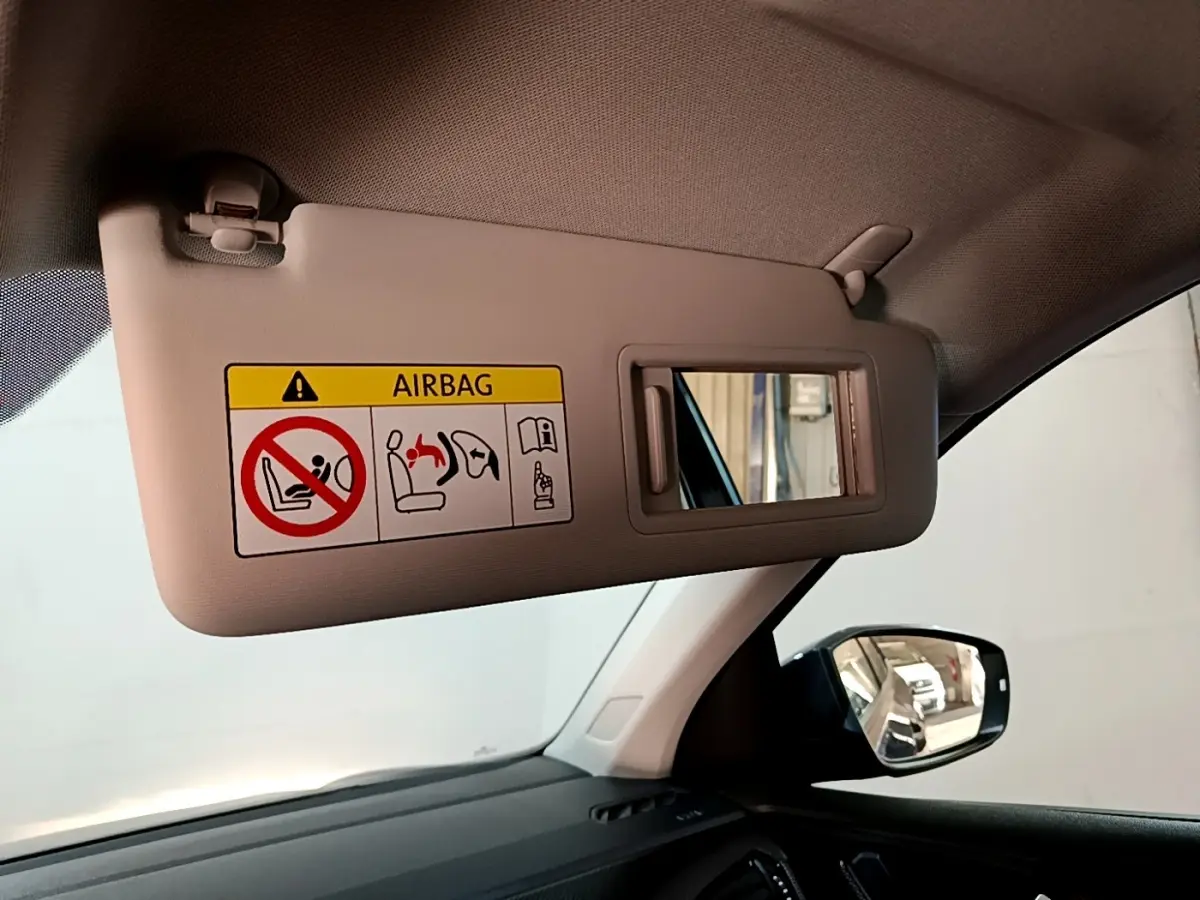 Vue intérieure côté gauche du pare-soleil beige avec miroir et avertissement airbag du Volkswagen T-Cross gris foncé 2023.