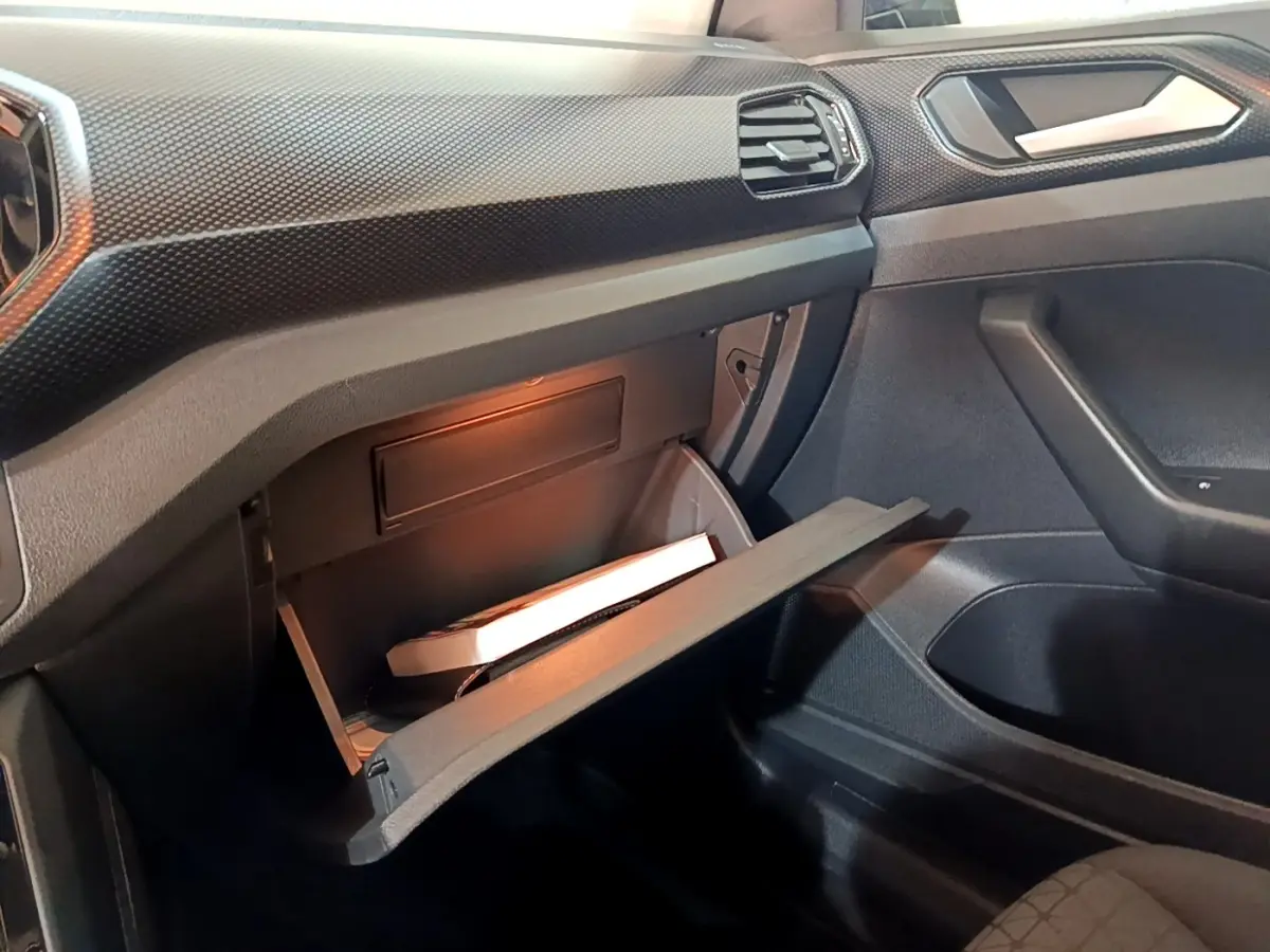 Vue intérieure côté passager du Volkswagen T-Cross 2023 gris foncé, boîte à gants ouverte avec éclairage intérieur.