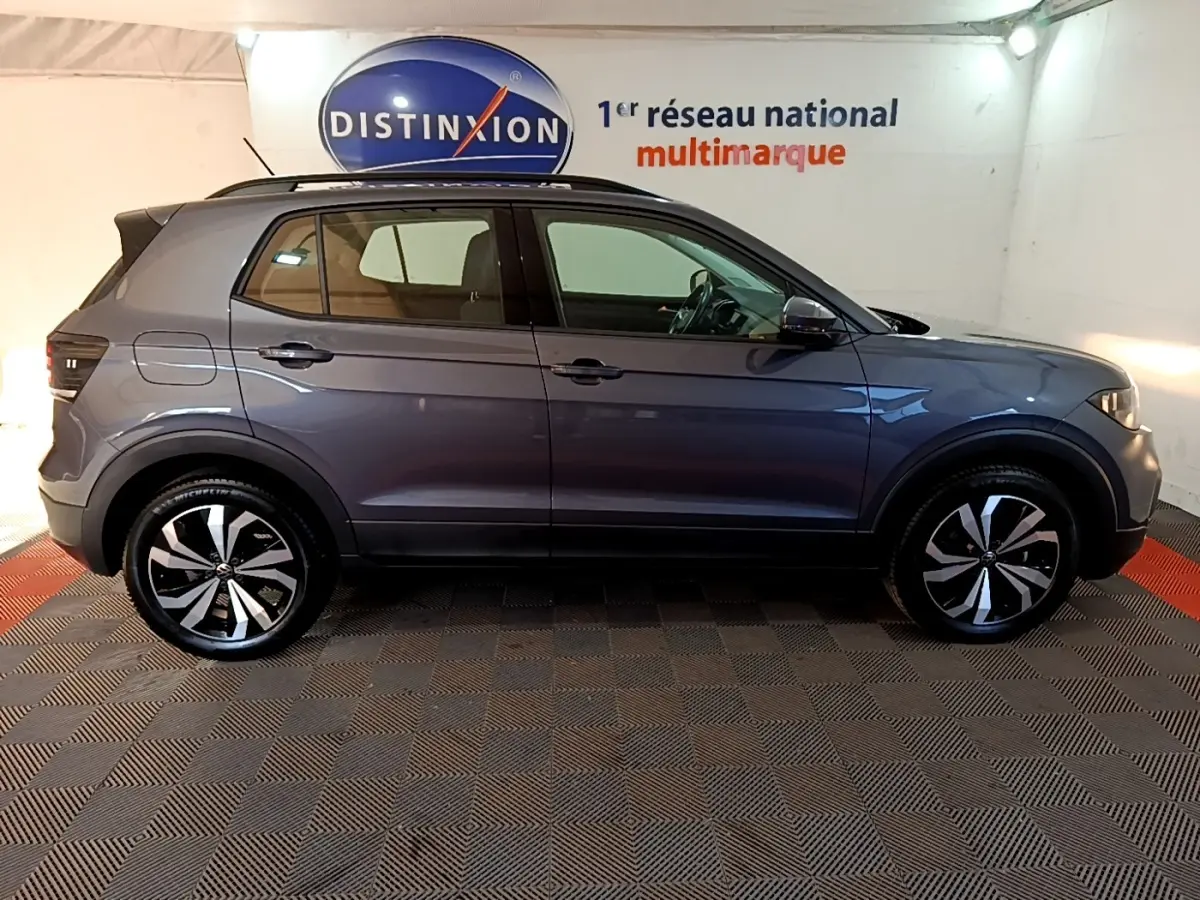 Profil côté gauche d'un Volkswagen T-Cross gris foncé 2023 avec jantes alliage distinctives dans un showroom.