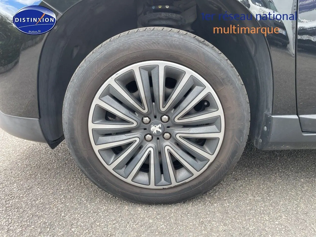 Gros plan sur la roue avant gauche d'un Peugeot 2008 noir métal, mettant en valeur la jante au design moderne.