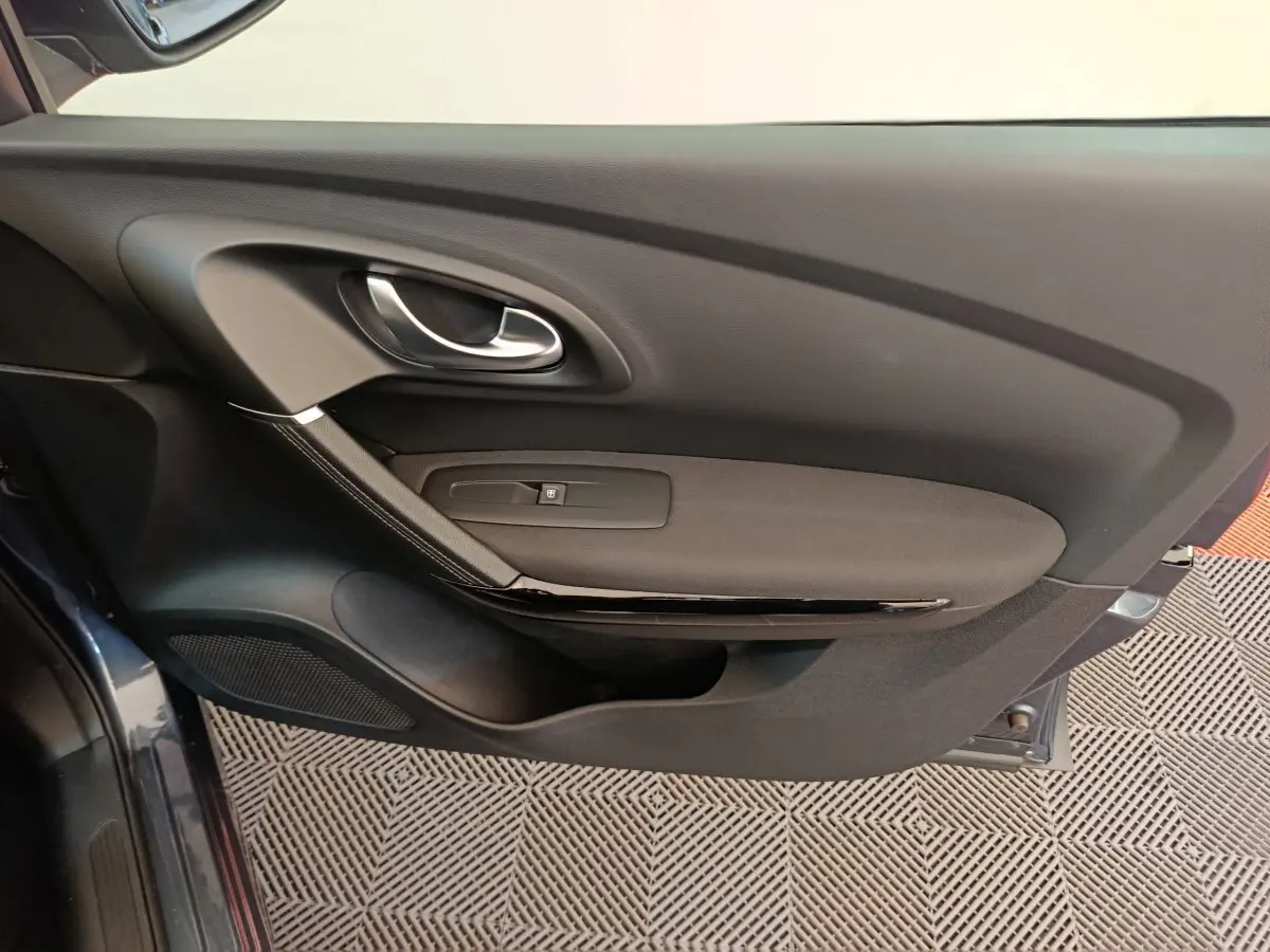 Intérieur de la porte côté gauche du Renault Kadjar gris foncé, avec poignée argentée et commande de vitre.