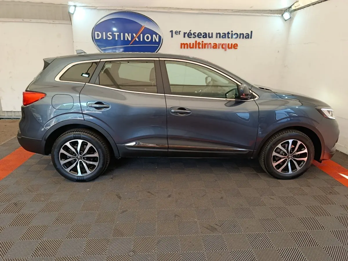 Profil côté gauche d'un Renault Kadjar Business gris foncé, stationné en intérieur avec jantes alliage et logo Distinxion en arrière-plan.
