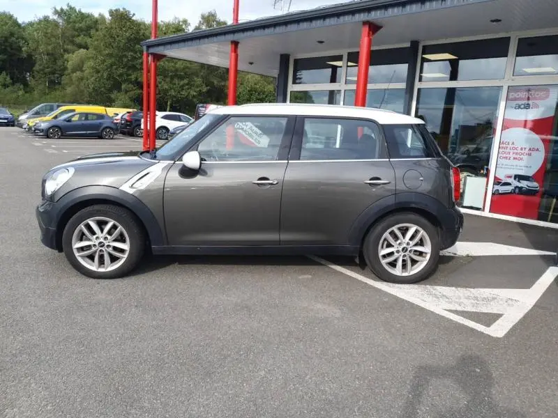 Profil droit d'une MINI Countryman Cooper D 2014 en Royal Grey avec toit blanc et jantes alu, stationnée devant un bâtiment.