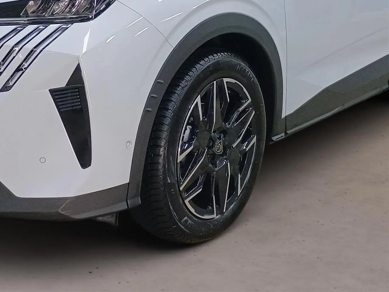 Gros plan sur la roue avant droite et l'aile blanche du Peugeot 3008 Hybrid 145 e-DSC6 Allure avec jante alliage noire et argent.