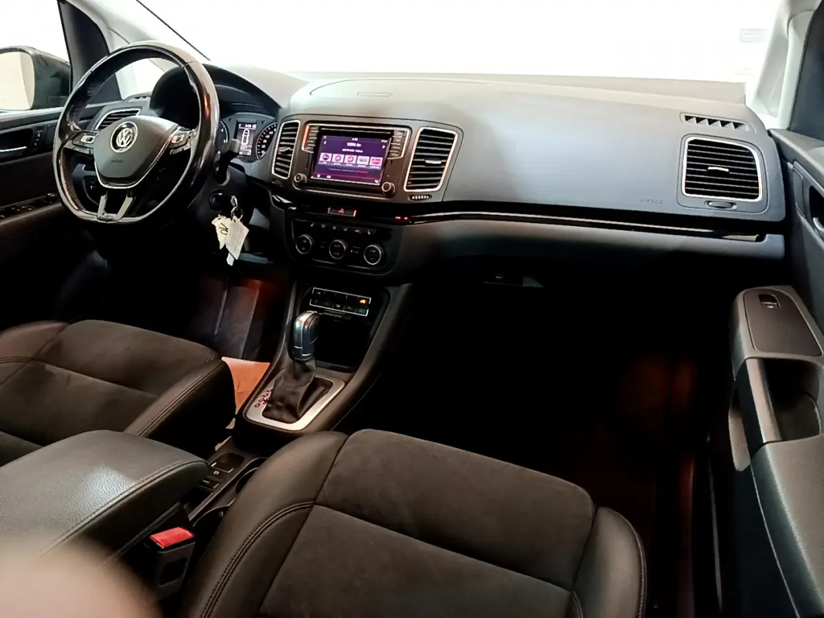 Vue intérieure côté conducteur du Volkswagen Sharan 2017, tableau de bord noir avec écran tactile et volant cuir multifonctions.