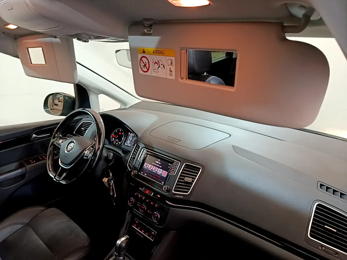 Vue intérieure côté conducteur du Volkswagen Sharan 2017, tableau de bord noir avec écran tactile et volant cuir.