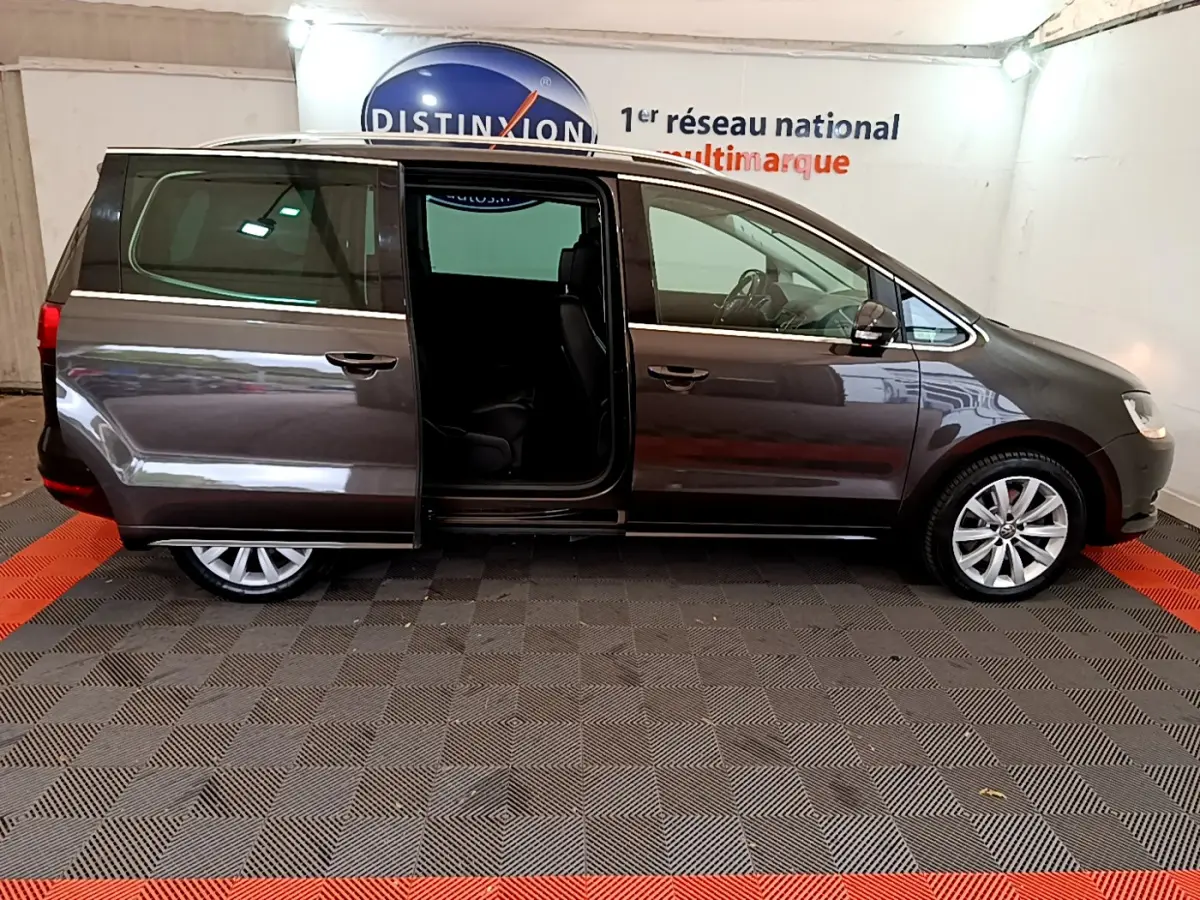 Vue latérale droite d’un Volkswagen Sharan marron 2017 avec porte coulissante arrière ouverte en intérieur showroom.