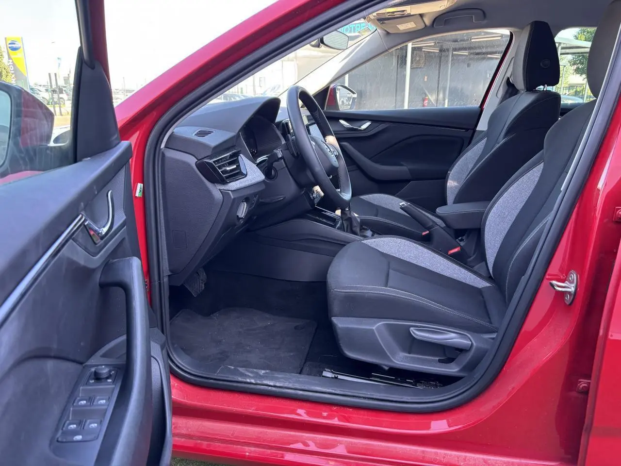 Intérieur côté conducteur d'une Skoda Scala rouge velvet metal 2024, sièges tissu noir et gris, volant multifonctions visible.