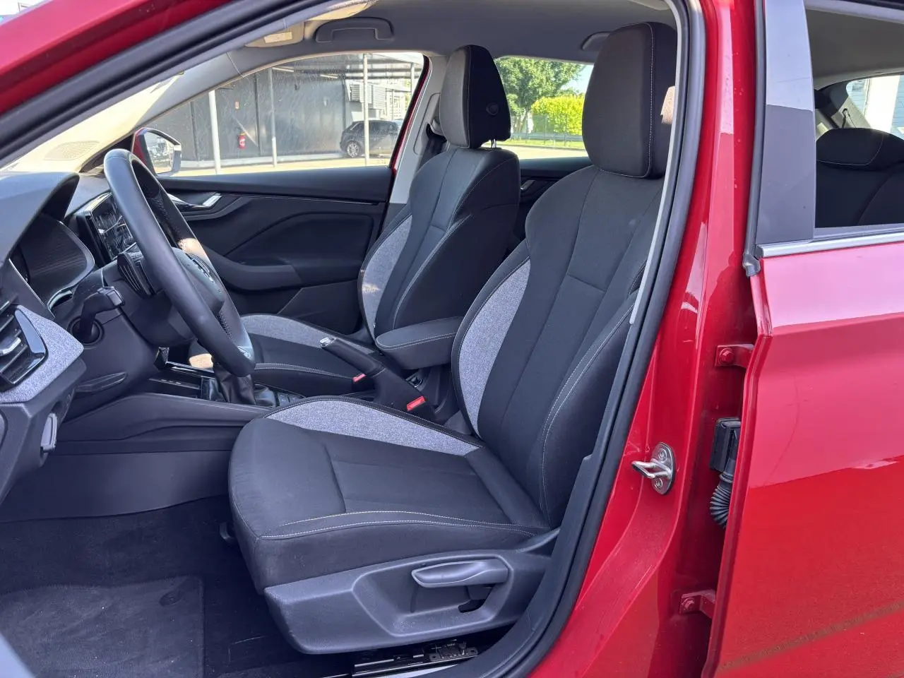 Intérieur avant droit d'une Skoda Scala 2024 rouge velvet metal, sièges tissu noir et gris avec surpiqûres claires.