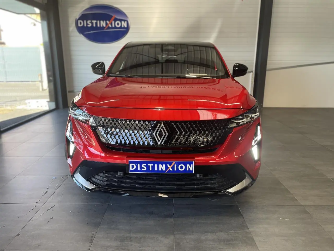 Vue frontale du Renault Rafale 2025 rouge à toit noir avec calandre noire et feux LED allumés en showroom.