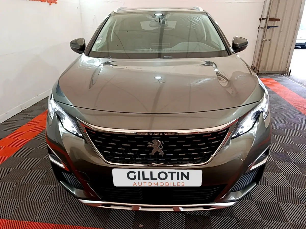 Vue frontale d'un Peugeot 3008 gris clair avec calandre chromée et phares LED allumés dans un garage.