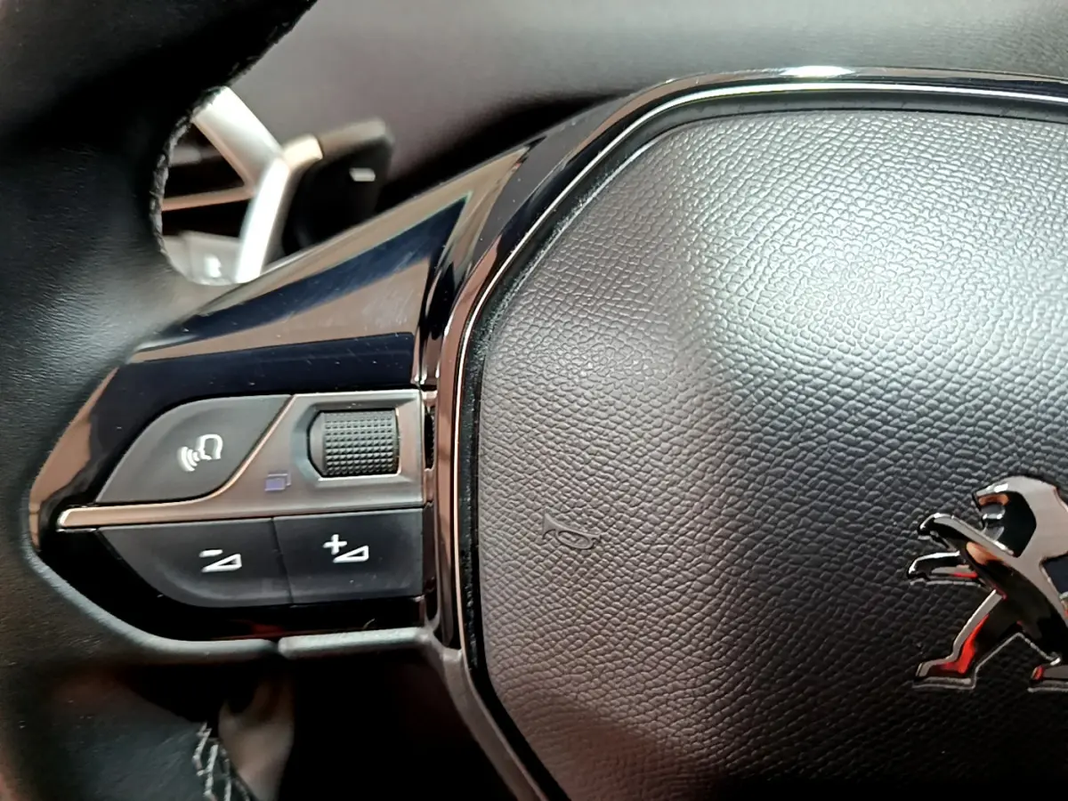 Gros plan sur le volant cuir noir du Peugeot 3008 2020 avec commandes vocales et logo lion chromé visible.