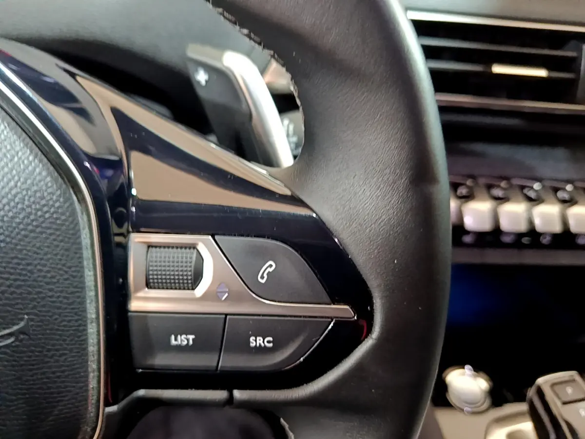 Gros plan sur les commandes gauche du volant cuir noir du Peugeot 3008 gris clair, avec tableau de bord en arrière-plan.