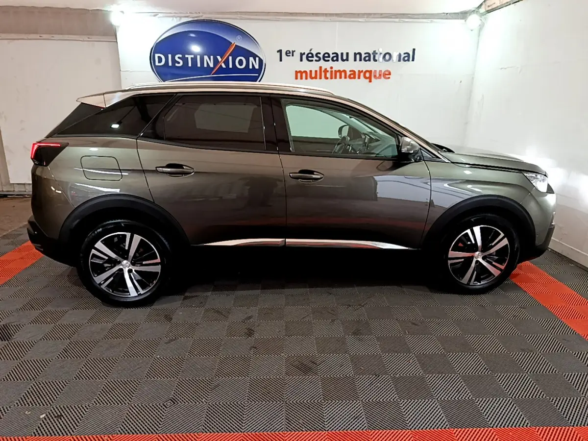 Profil côté gauche du Peugeot 3008 gris clair 2020, avec jantes alliage et vitres teintées en arrière-plan showroom.