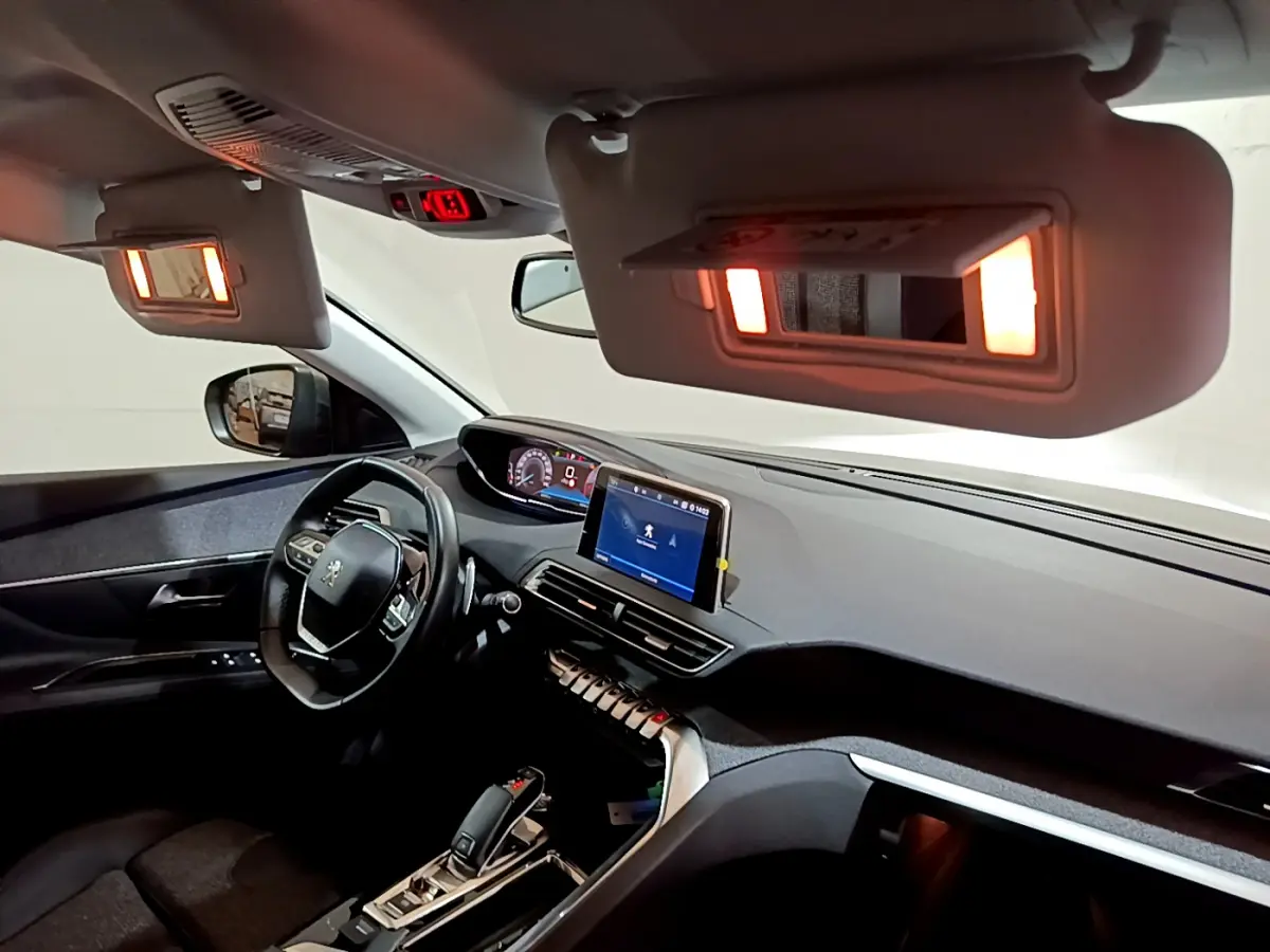 Intérieur du Peugeot 3008 gris clair vu côté conducteur, tableau de bord moderne avec écran tactile allumé et miroirs de courtoisie éclairés.