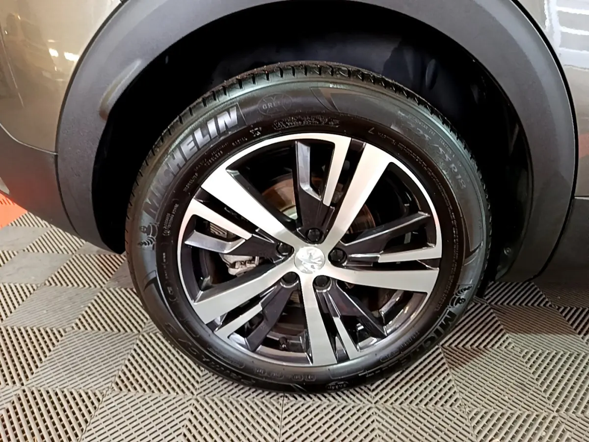 Gros plan sur la roue avant droite du Peugeot 3008 gris clair, mettant en valeur la jante alliage et le pneu Michelin.