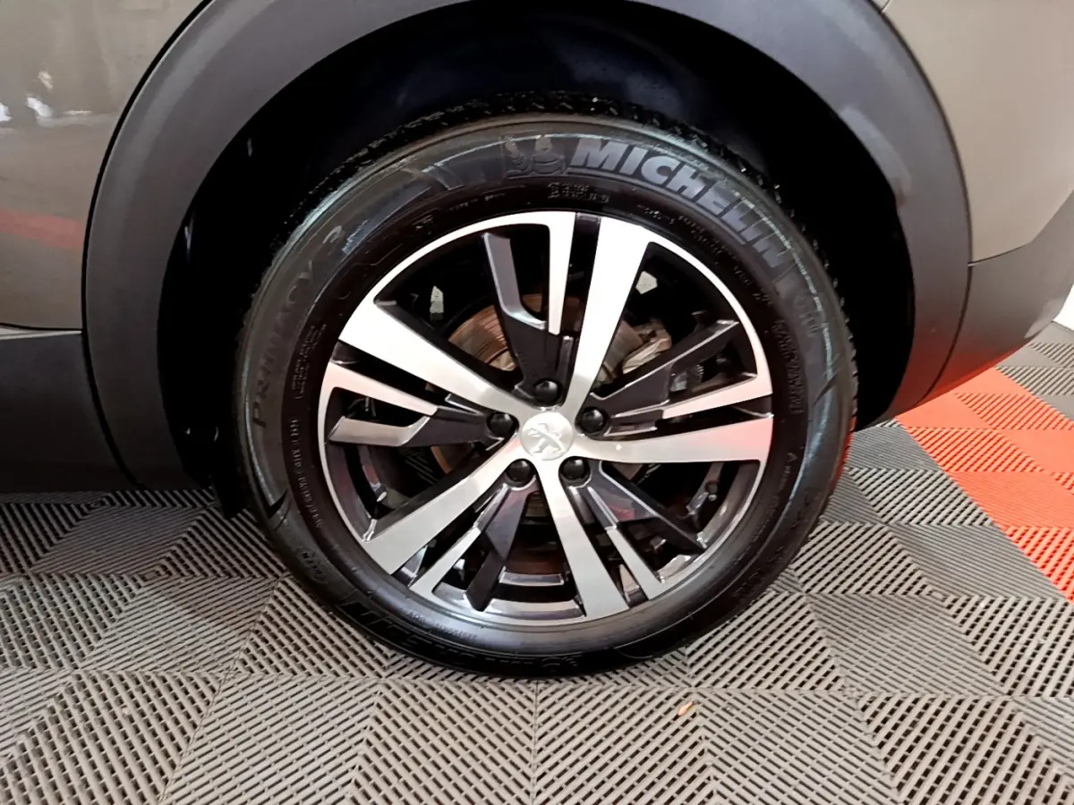 Gros plan sur la roue avant droite du Peugeot 3008 gris clair, jante alliage bicolore et pneu Michelin visible.