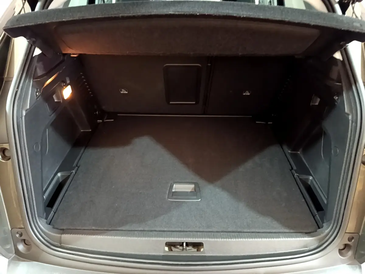 Coffre ouvert vu de l'arrière d'un Peugeot 3008 gris clair, avec espace de chargement propre et éclairage latéral allumé.