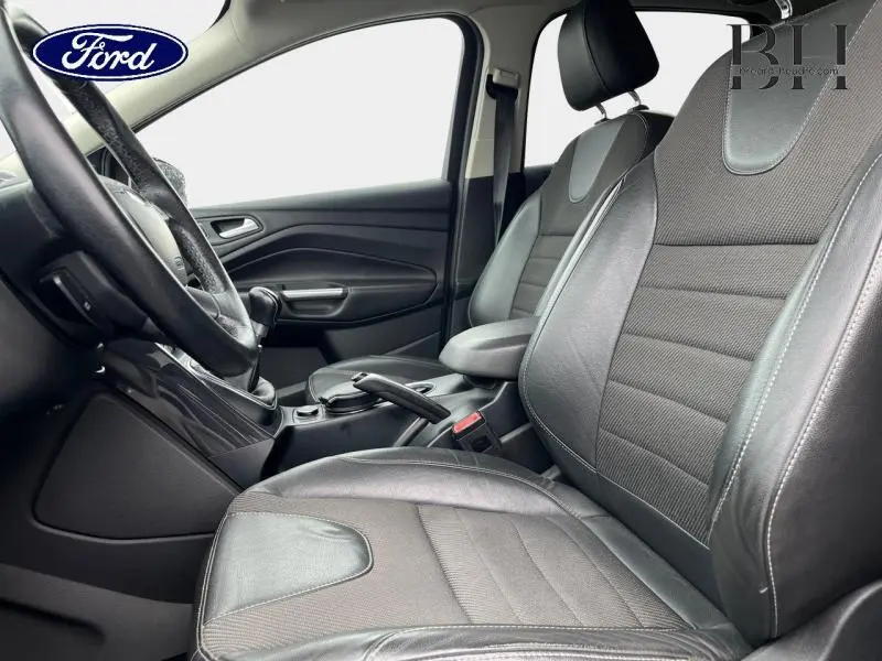 Intérieur avant du Ford Kuga gris Magnetic de 2015, sièges sport en cuir et tissu, volant multifonction en cuir visible de côté gauche.