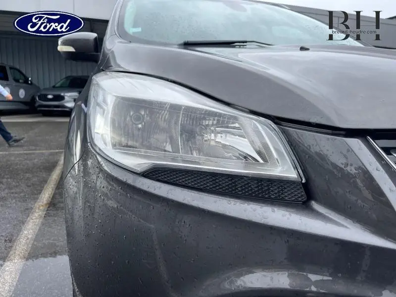 Gros plan sur le phare avant gauche du Ford Kuga gris Magnetic 2015, avec gouttes de pluie visibles sur la carrosserie.