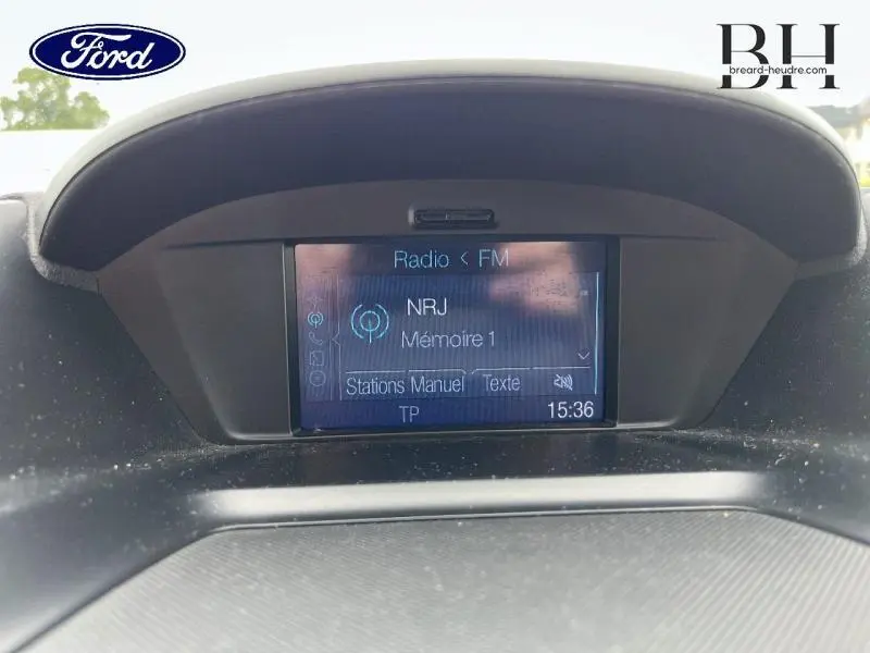 Écran multifonction central du Ford Kuga 2015 affichant la radio FM NRJ, avec tableau de bord noir en arrière-plan.
