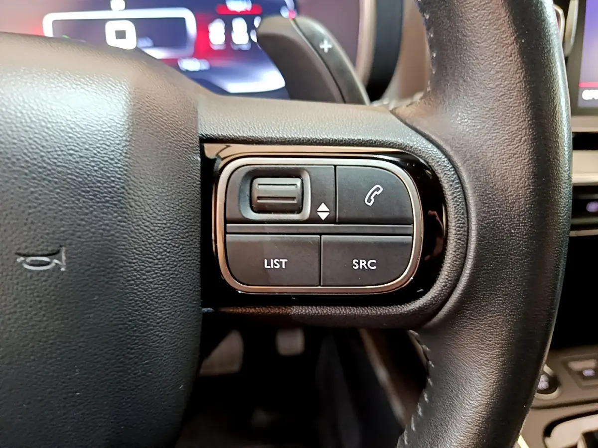 Gros plan sur les commandes gauche du volant cuir du Citroën C5 Aircross noir, avec affichage numérique en arrière-plan.