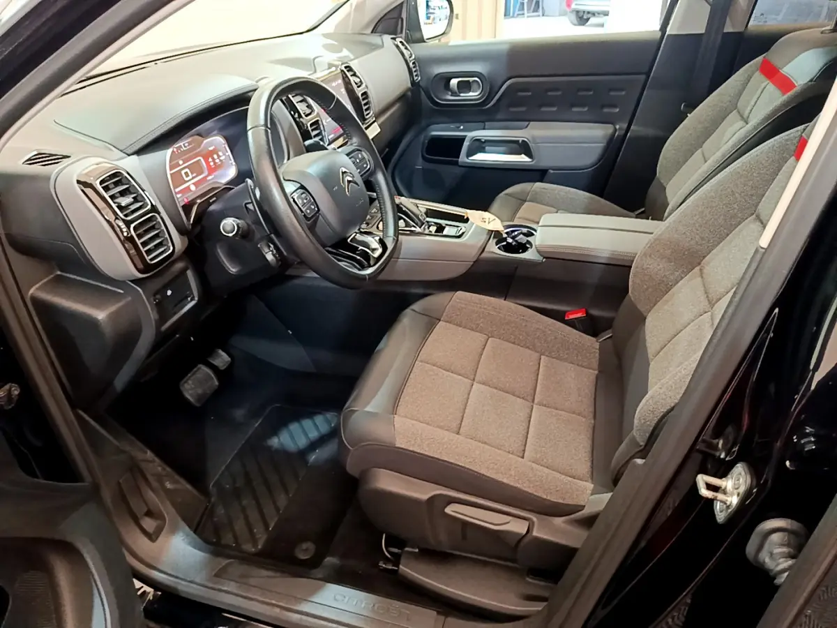 Intérieur côté conducteur du Citroën C5 Aircross noir, montrant le tableau de bord et sièges gris avec accoudoir central.