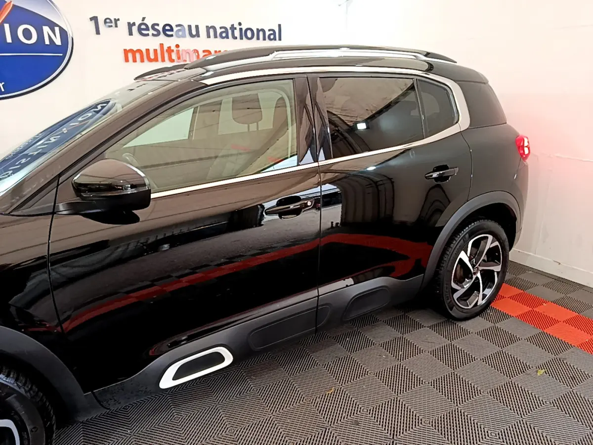 Profil côté gauche du Citroën C5 Aircross noir 2020 avec jantes alliage et barres de toit visibles en intérieur showroom.