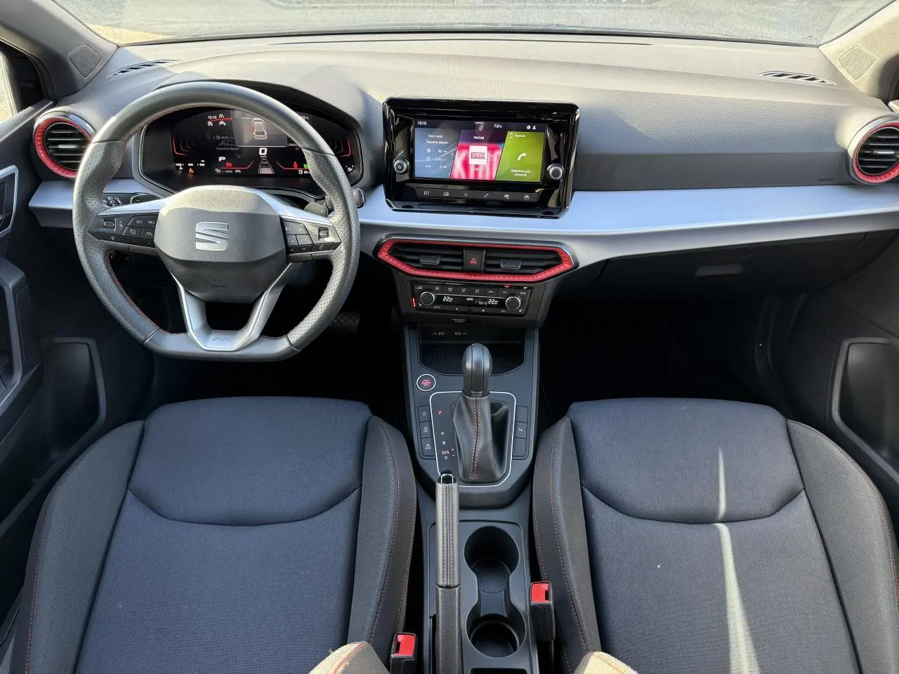 Vue intérieure frontale du tableau de bord et des sièges noirs de la SEAT IBIZA 2024 avec volant sport et écran tactile central.
