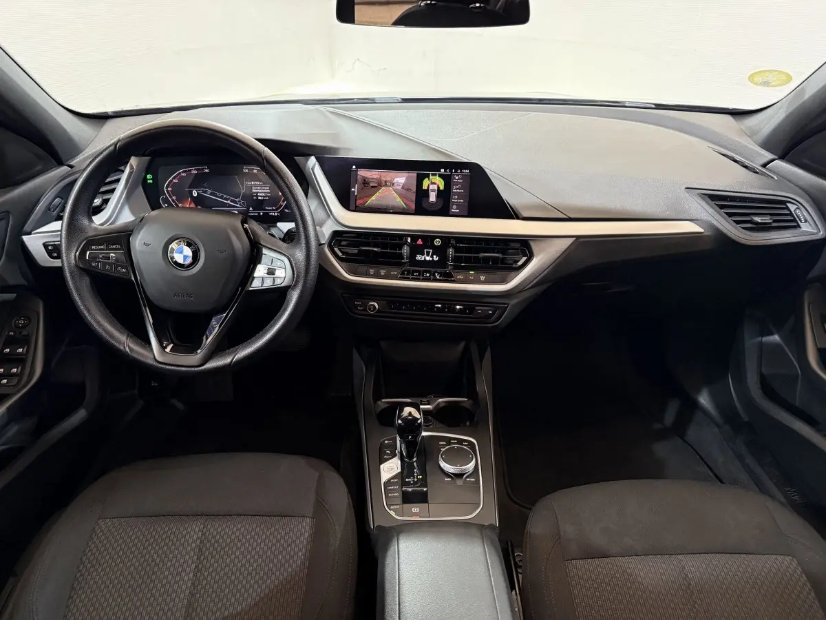 Vue intérieure avant de la BMW Série 1 116d Business Design 2022, tableau de bord noir avec écran tactile et volant cuir multifonctions.