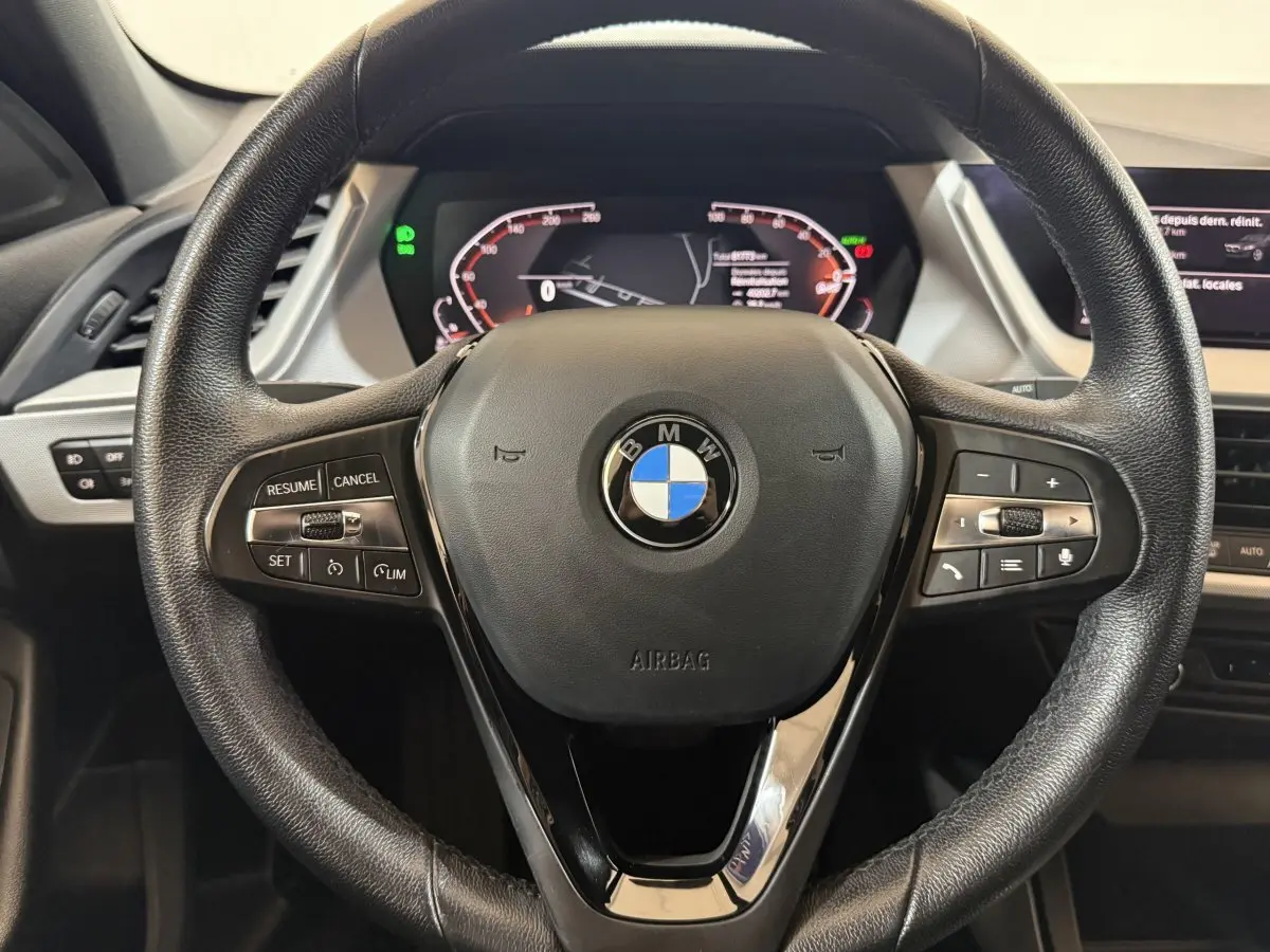 Vue rapprochée du volant cuir noir BMW Série 1 116d 2022 avec commandes multifonctions et tableau de bord digital.