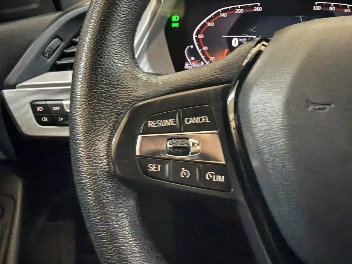 Gros plan sur le côté gauche du volant cuir noir d'une BMW Série 1 116d 2022 avec commandes du régulateur de vitesse.