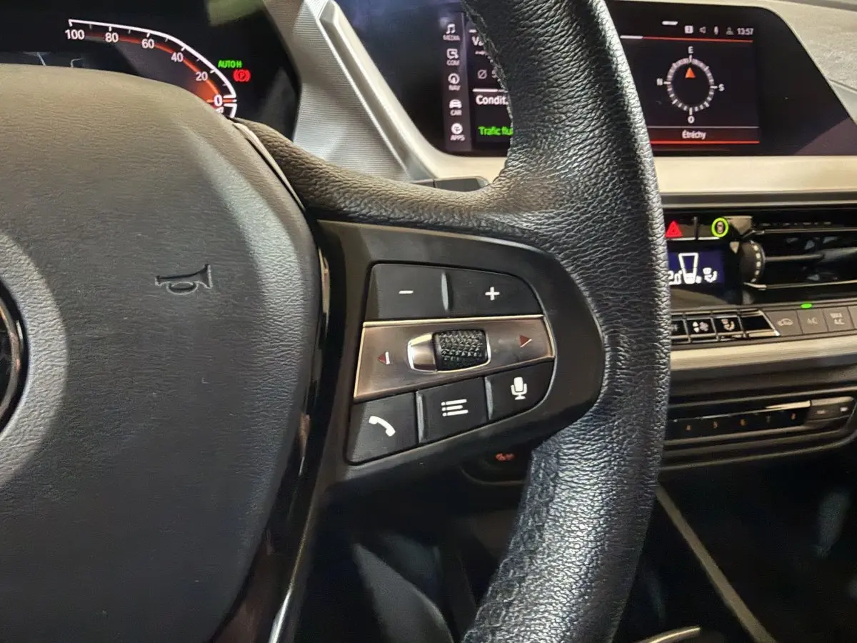 Gros plan sur le volant cuir noir de la BMW Série 1 116d avec commandes multifonctions et tableau de bord digital.