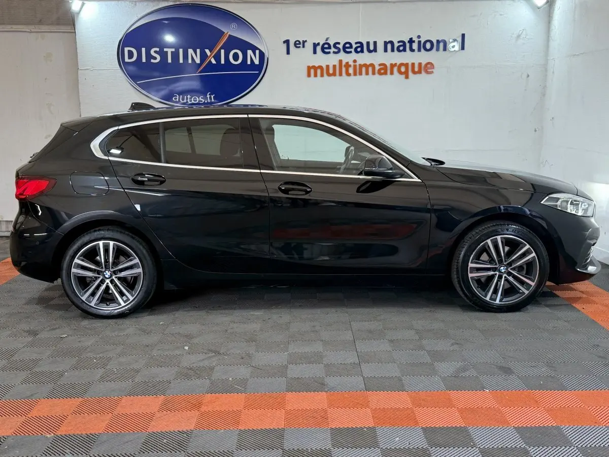 BMW Série 1 116d Business Design noire vue de profil côté gauche, avec jantes alliage et feux arrière allumés.