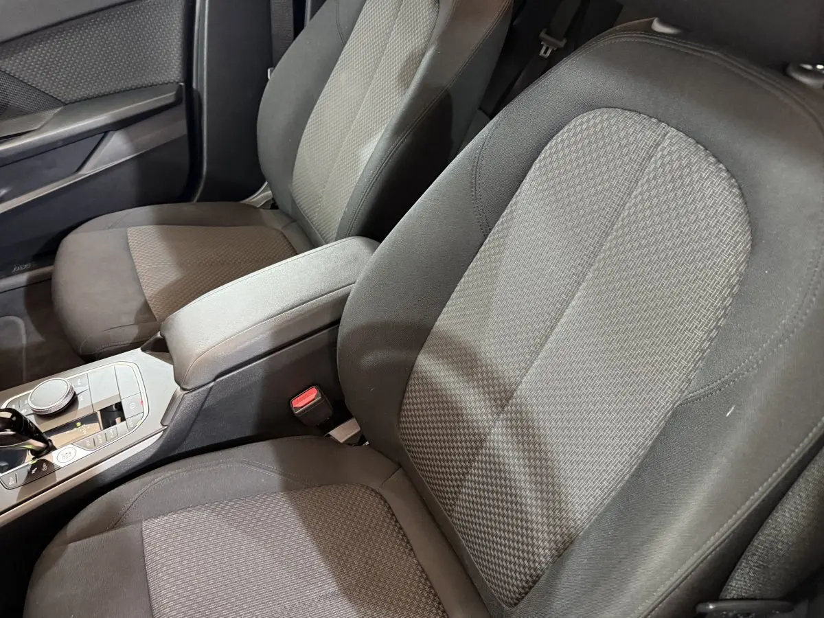 Vue rapprochée des sièges avant tissu gris et console centrale de la BMW Série 1 116d Business Design noire 2022.