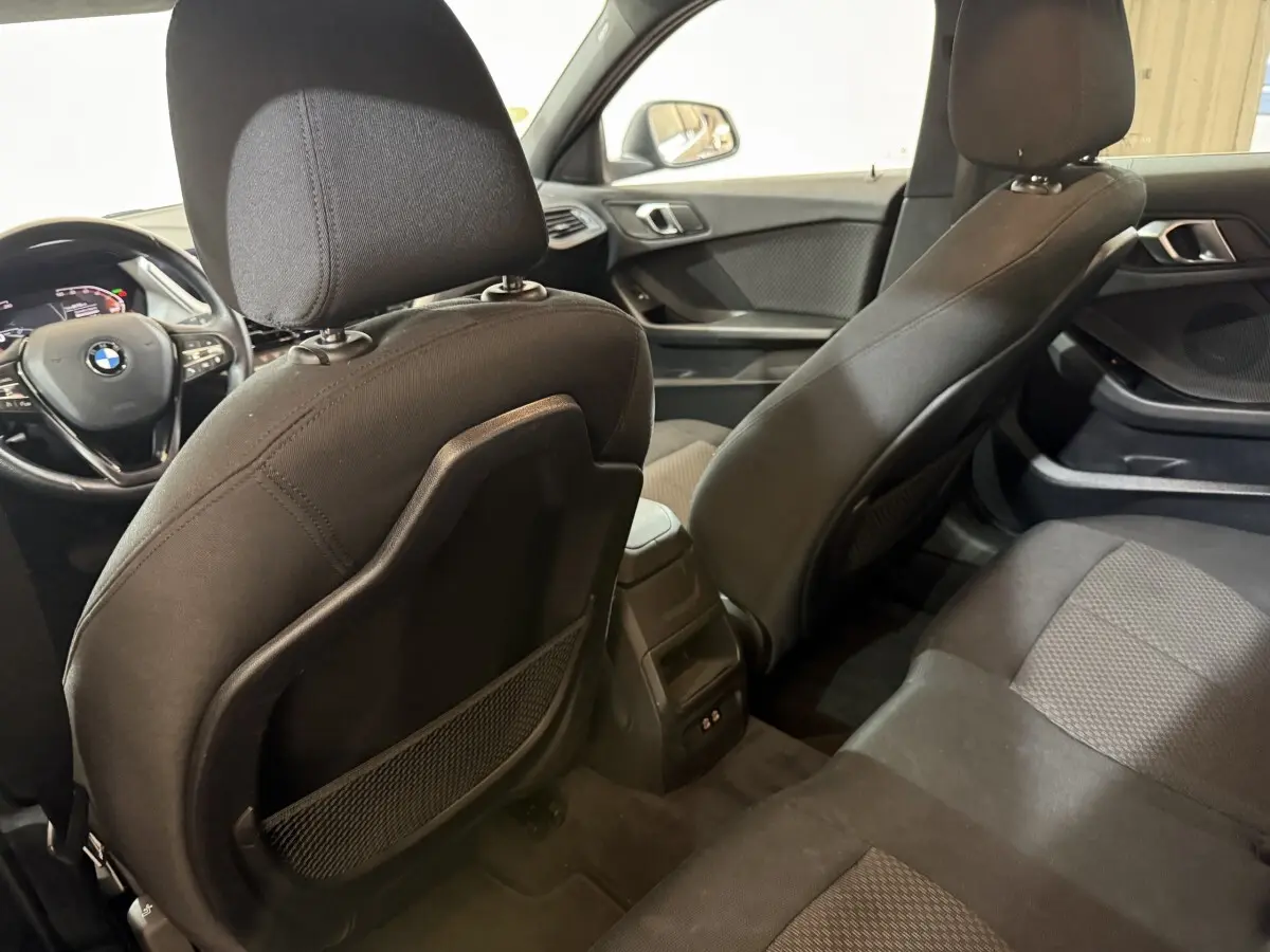 Vue intérieure arrière de la BMW Série 1 116d Business Design noire, montrant les sièges et le tableau de bord avant.