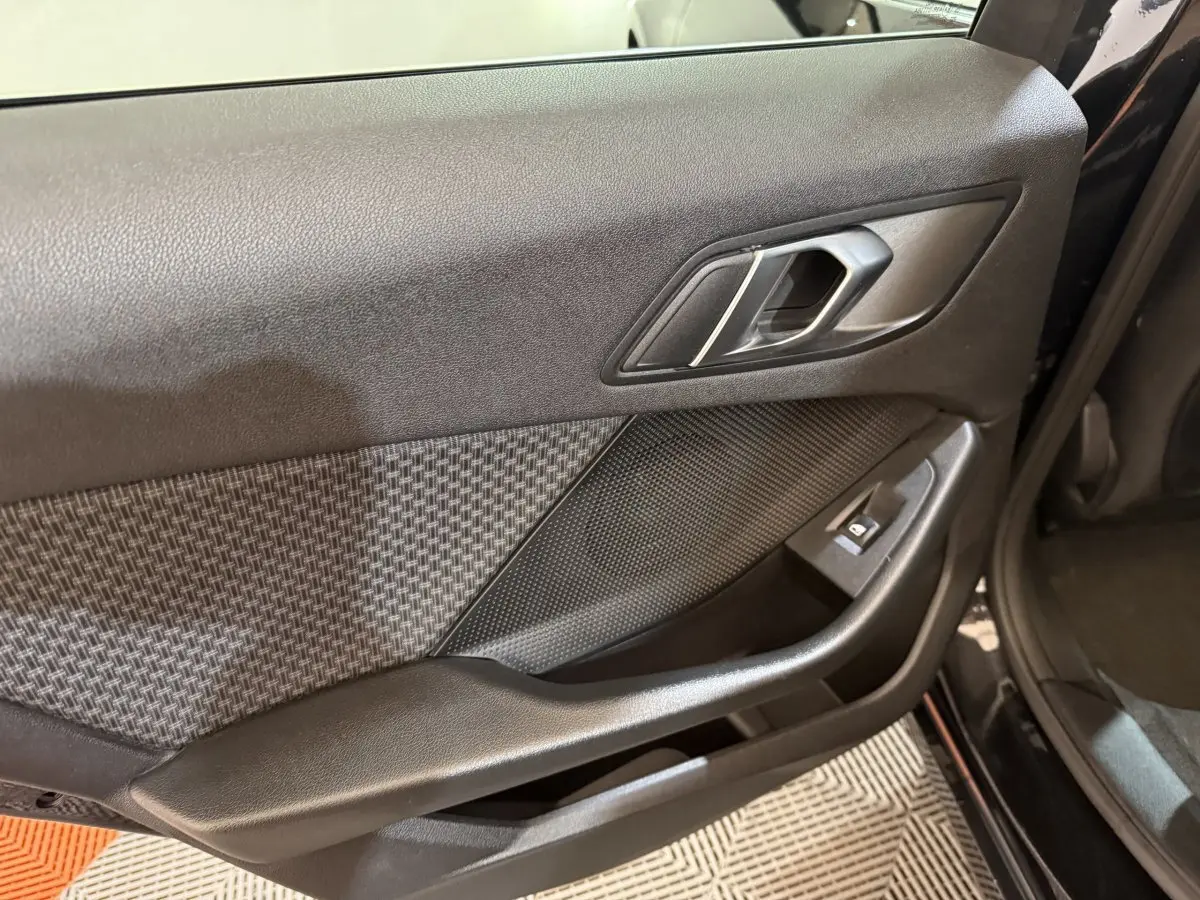 Vue intérieure côté gauche de la porte noire de la BMW Série 1 116d avec insert tissu à motif et commande de vitre.