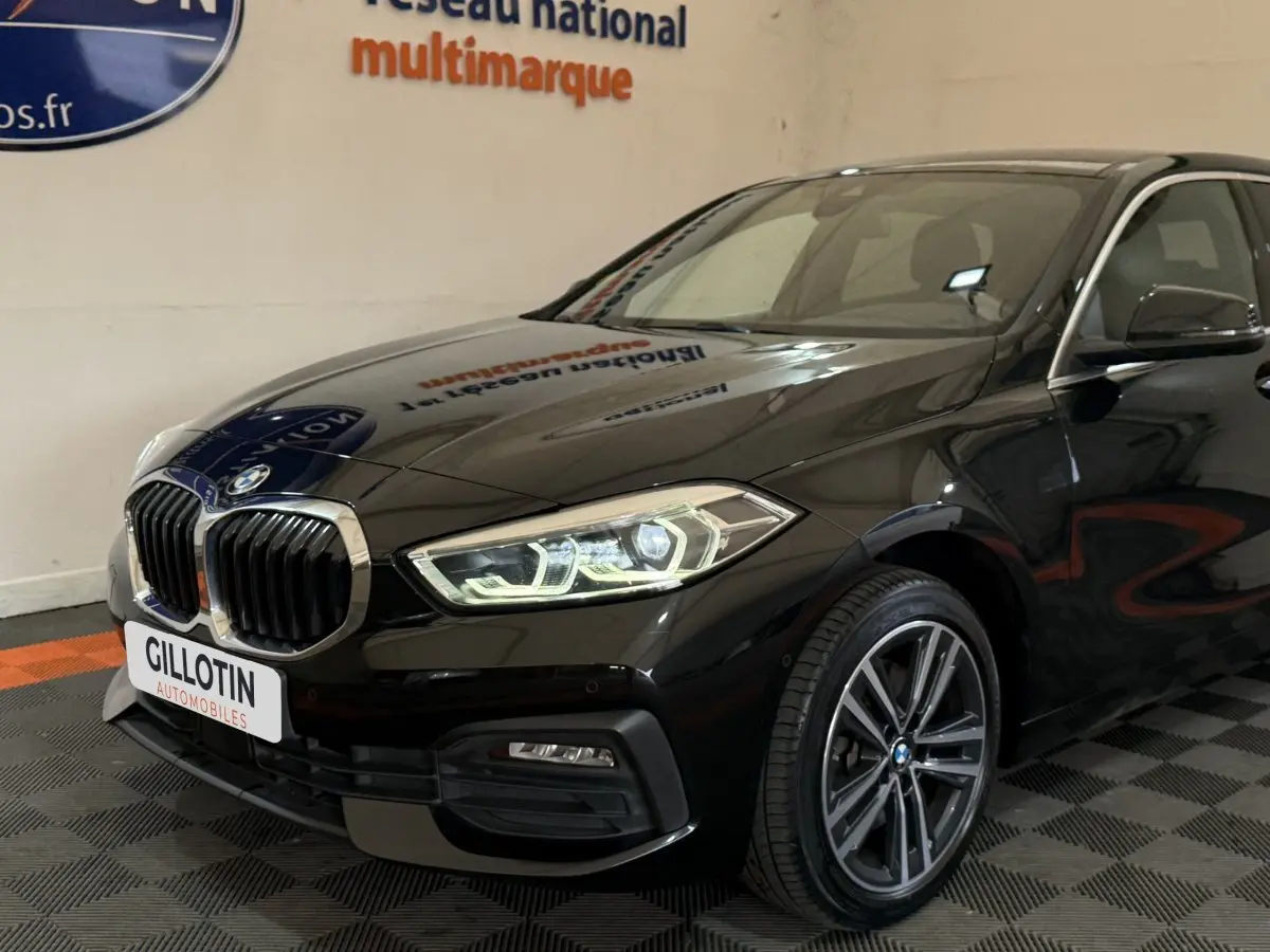 BMW Série 1 116d Business Design noire vue en 3/4 avant droit, avec phares LED et calandre chromée distinctive.