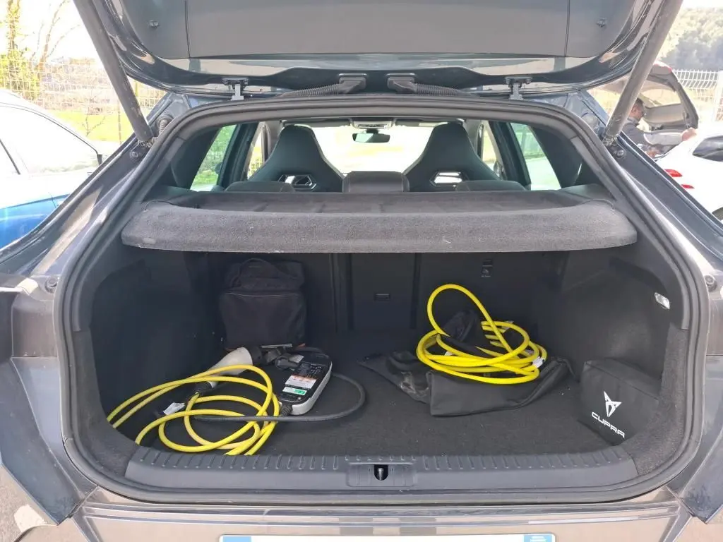 Coffre ouvert d'une CUPRA Formentor gris clair 2024, vue arrière, avec câbles de recharge jaune et sac de marque visible.