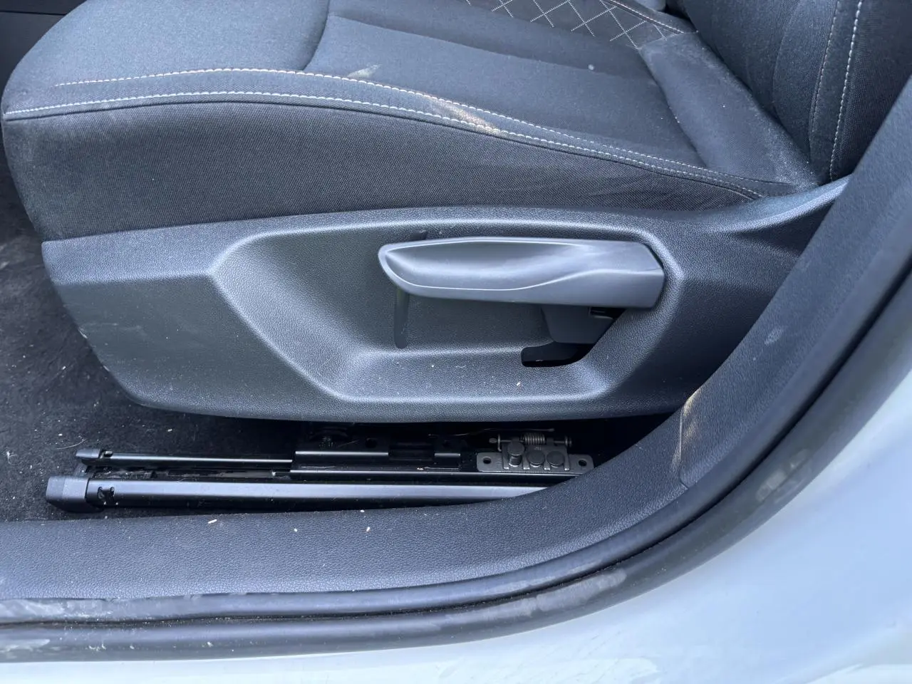 Gros plan sur la manette de réglage du siège conducteur noir de la Skoda Scala blanc glacier 2024, côté gauche.