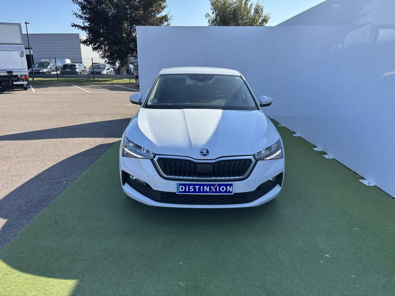 Vue frontale d'une Skoda Scala blanc glacier avec calandre noire et plaque Distinxion sur fond extérieur.