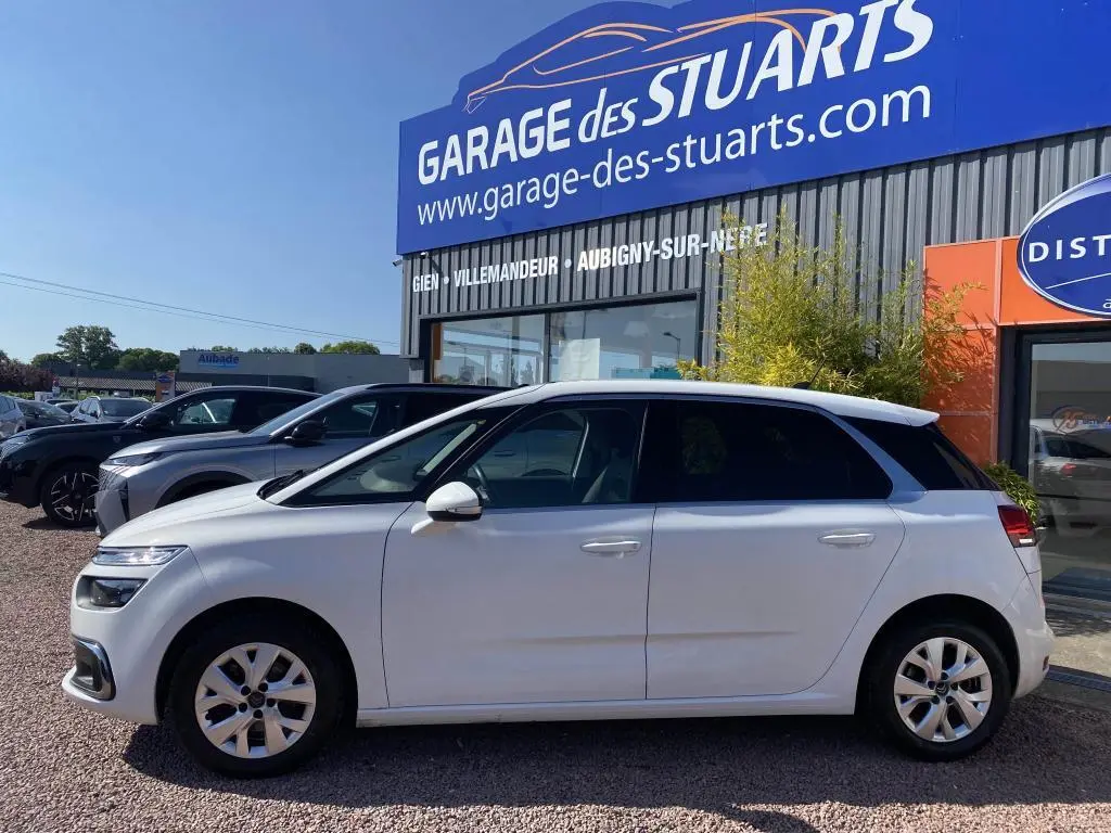 Vue de profil côté gauche d'une Citroën C4 Spacetourer blanche stationnée devant un garage.