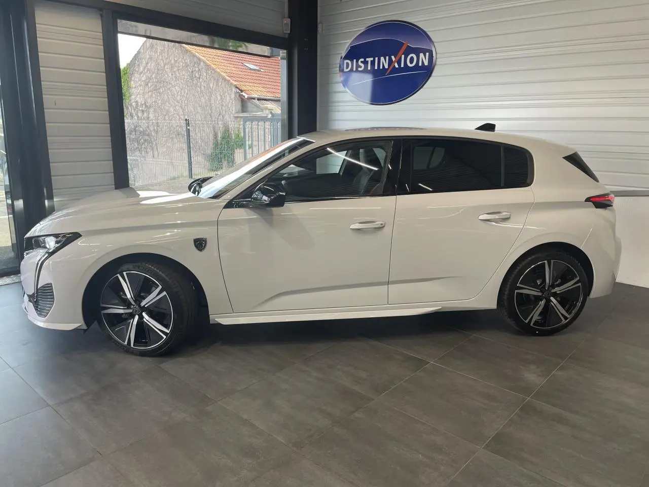 Profil côté gauche d'une Peugeot 308 blanche 2025 en finition GT avec jantes alliage noires et toit noir brillant.